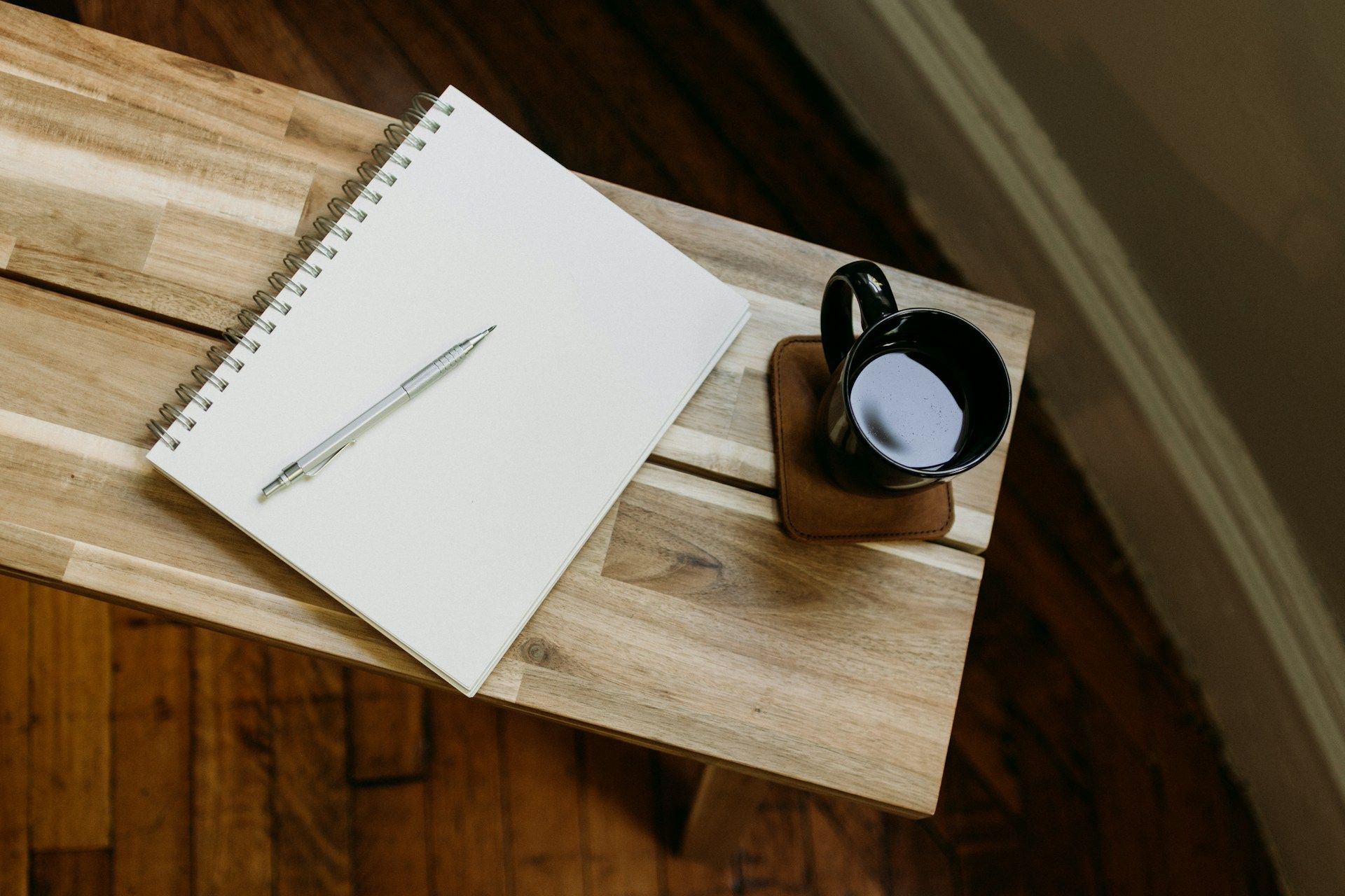 A notebook and a coffee cup on a wooden desk, arranged for a weekend planning session.