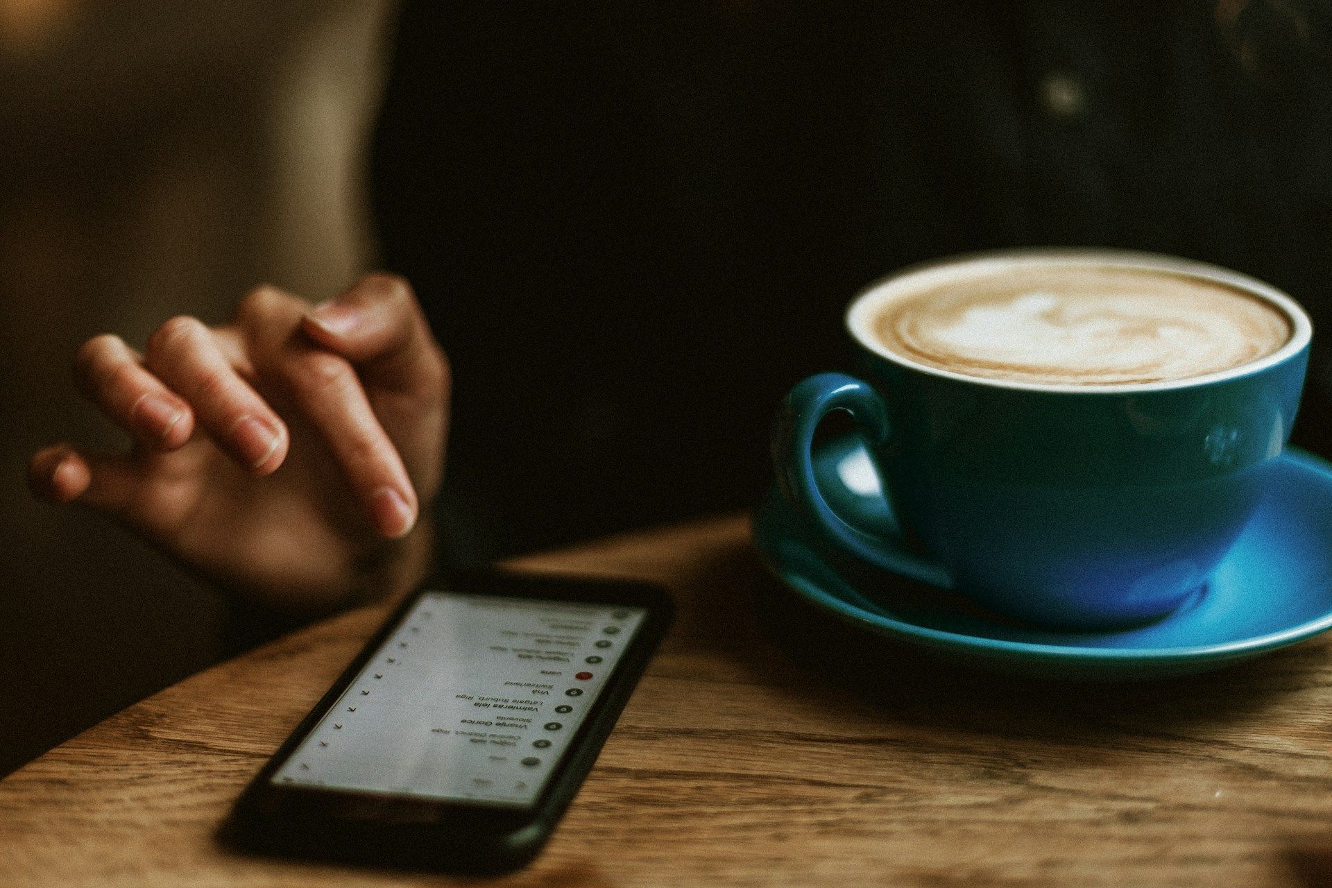 A person holding a phone at a kitchen table during a calm morning, mid-setup of an app.